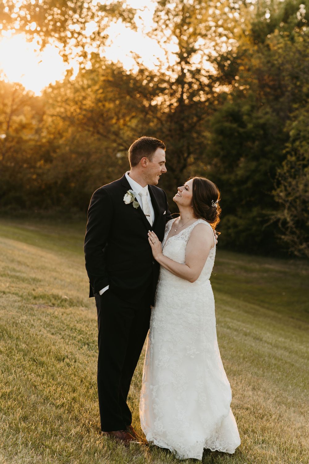 Bride and groom sharing a joyful moment gazing at each other during golden sunset outdoors.