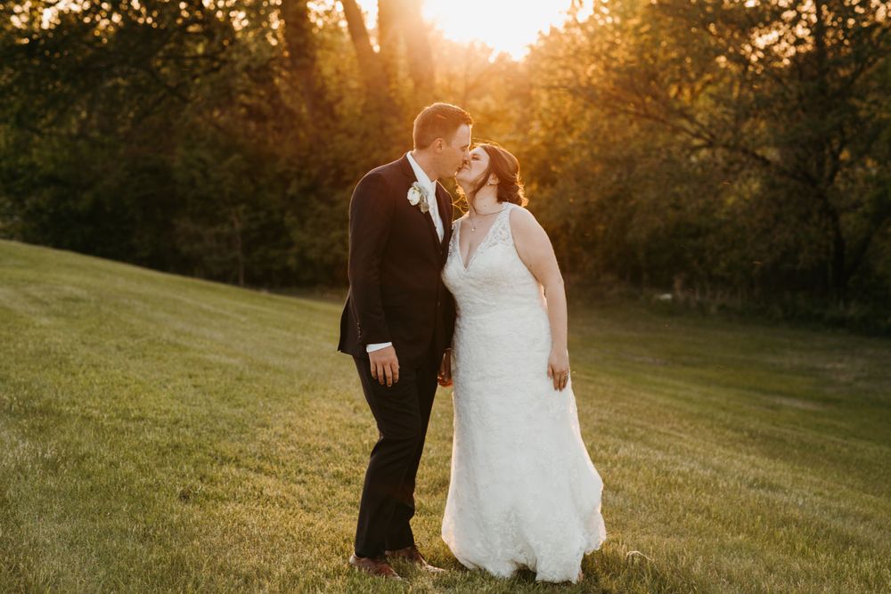Bride and groom sharing a tender kiss on green lawn bathed in golden sunset light.