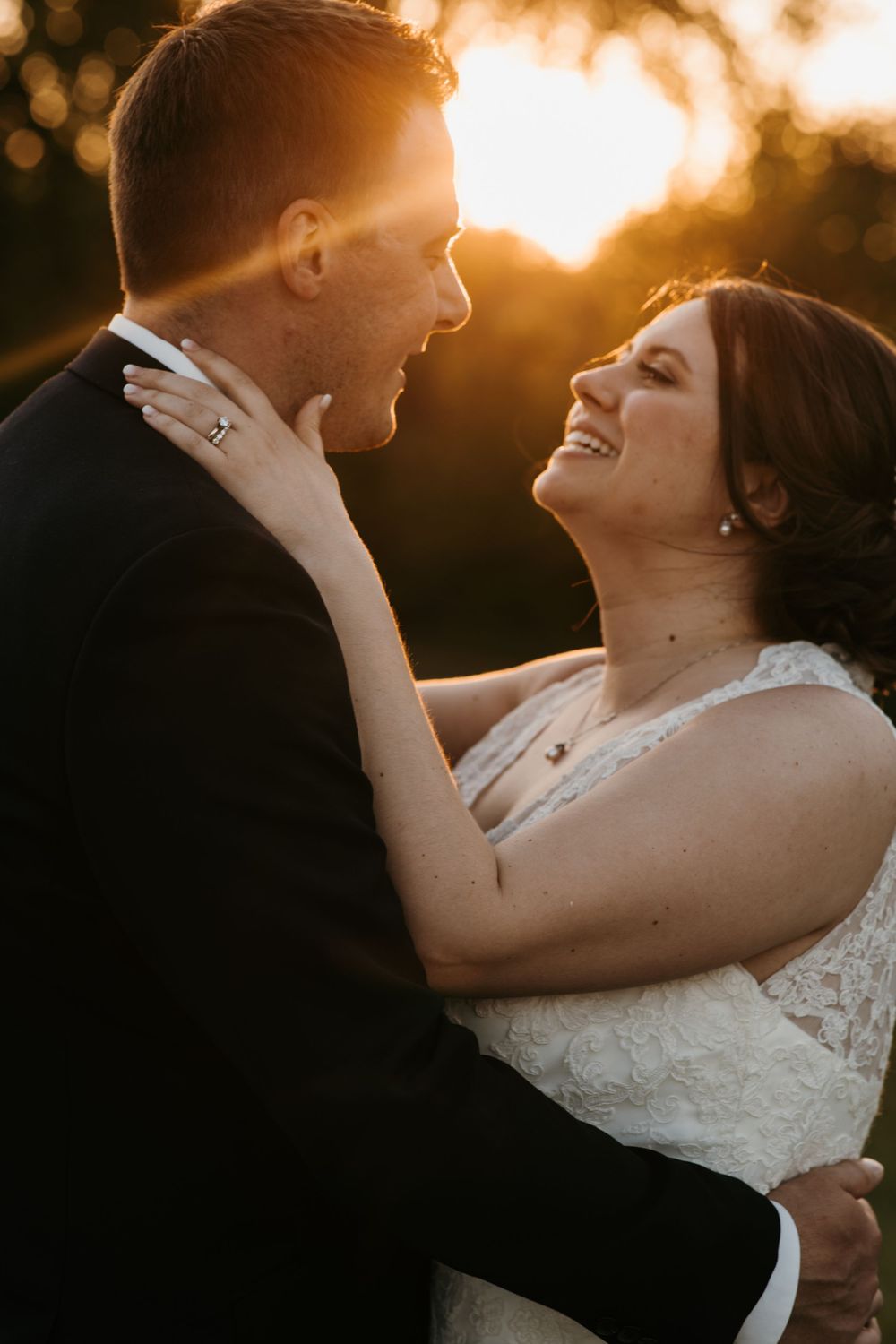 Bride laughing joyfully while holding grooms face during romantic golden hour wedding portrait.