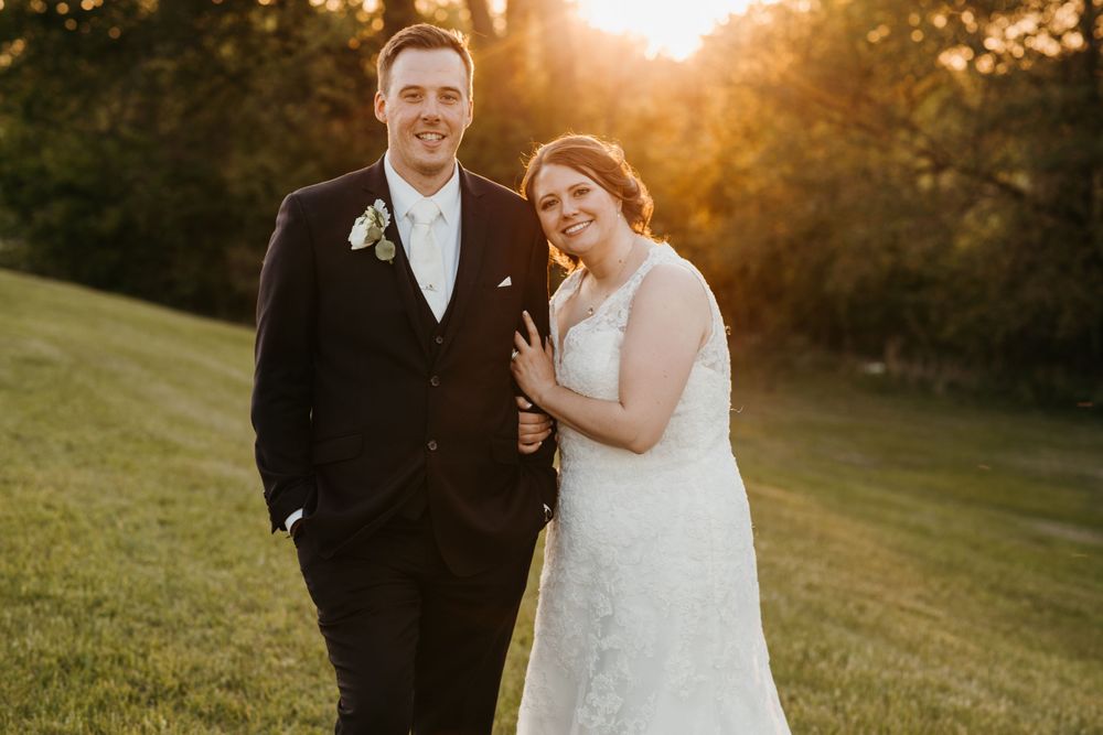 Smiling bride and groom pose together during golden hour sunset on their outdoor wedding day.