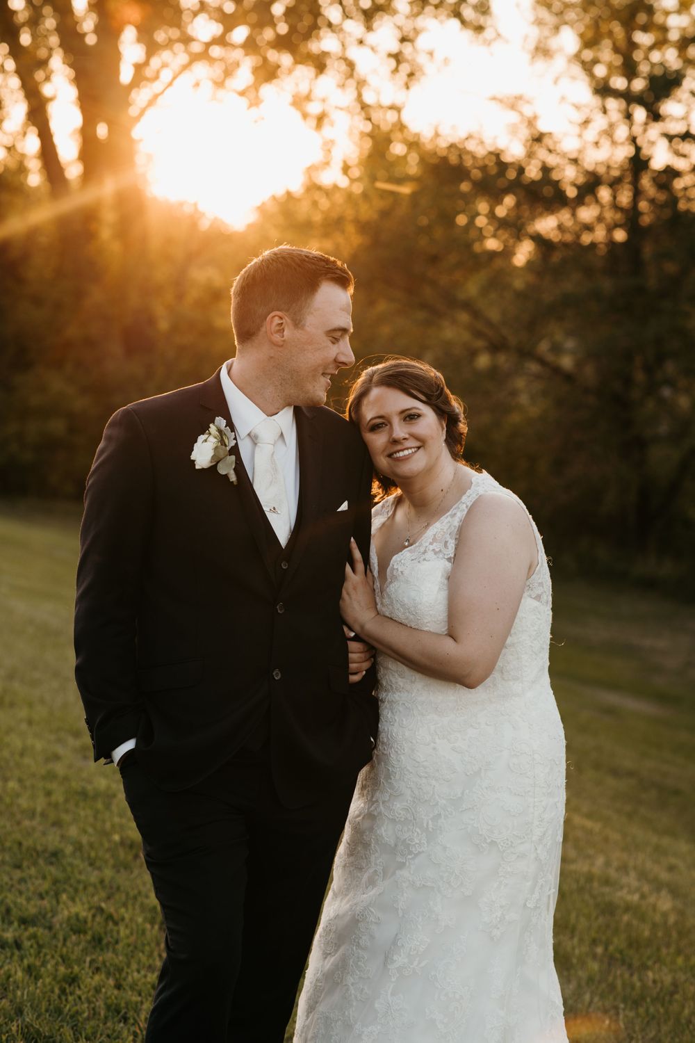 Bride and groom share a tender moment at golden hour sunset in a lush green outdoor wedding setting.
