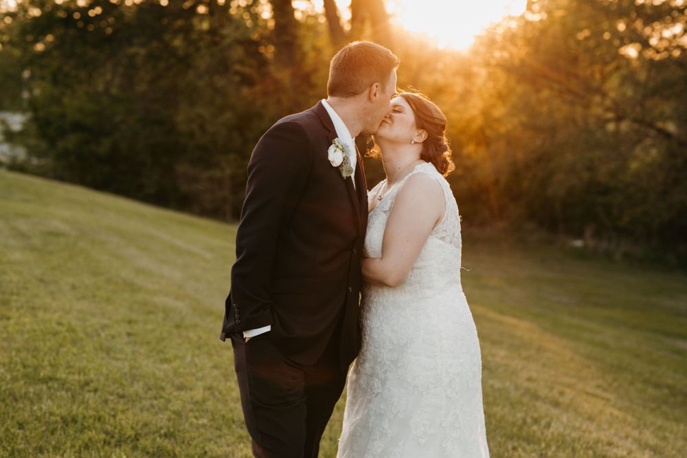 Bride and groom share a romantic kiss backlit by a stunning golden sunset on their wedding day.