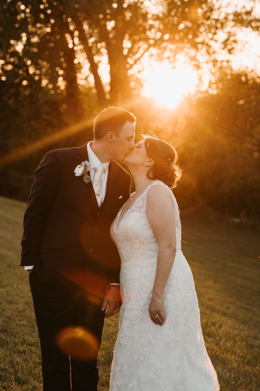 Bride and groom share a passionate kiss bathed in warm golden sunset light on their wedding day.