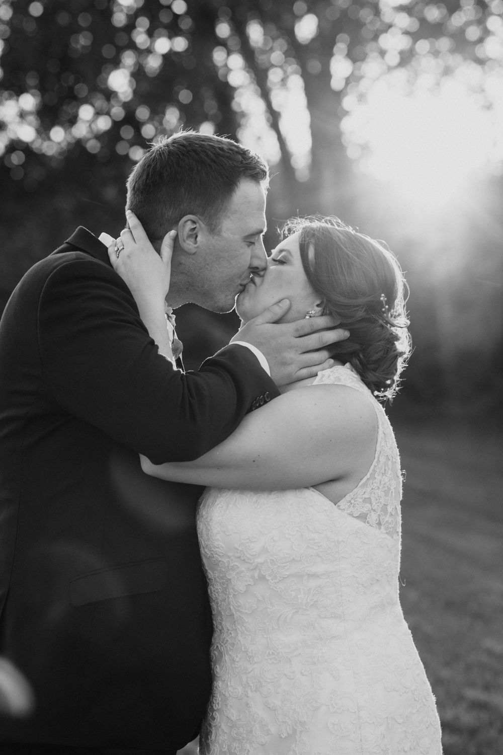 Black and white wedding portrait of bride and groom sharing an intimate kiss at golden hour.