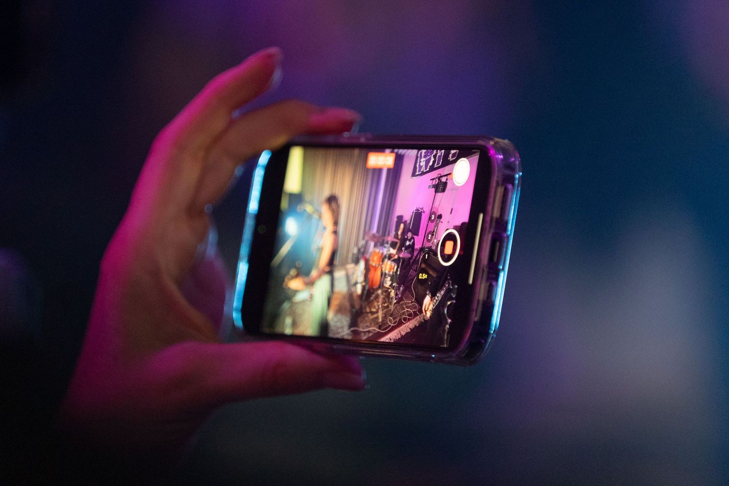 Hand holding smartphone capturing concert footage with pink and purple stage lighting.