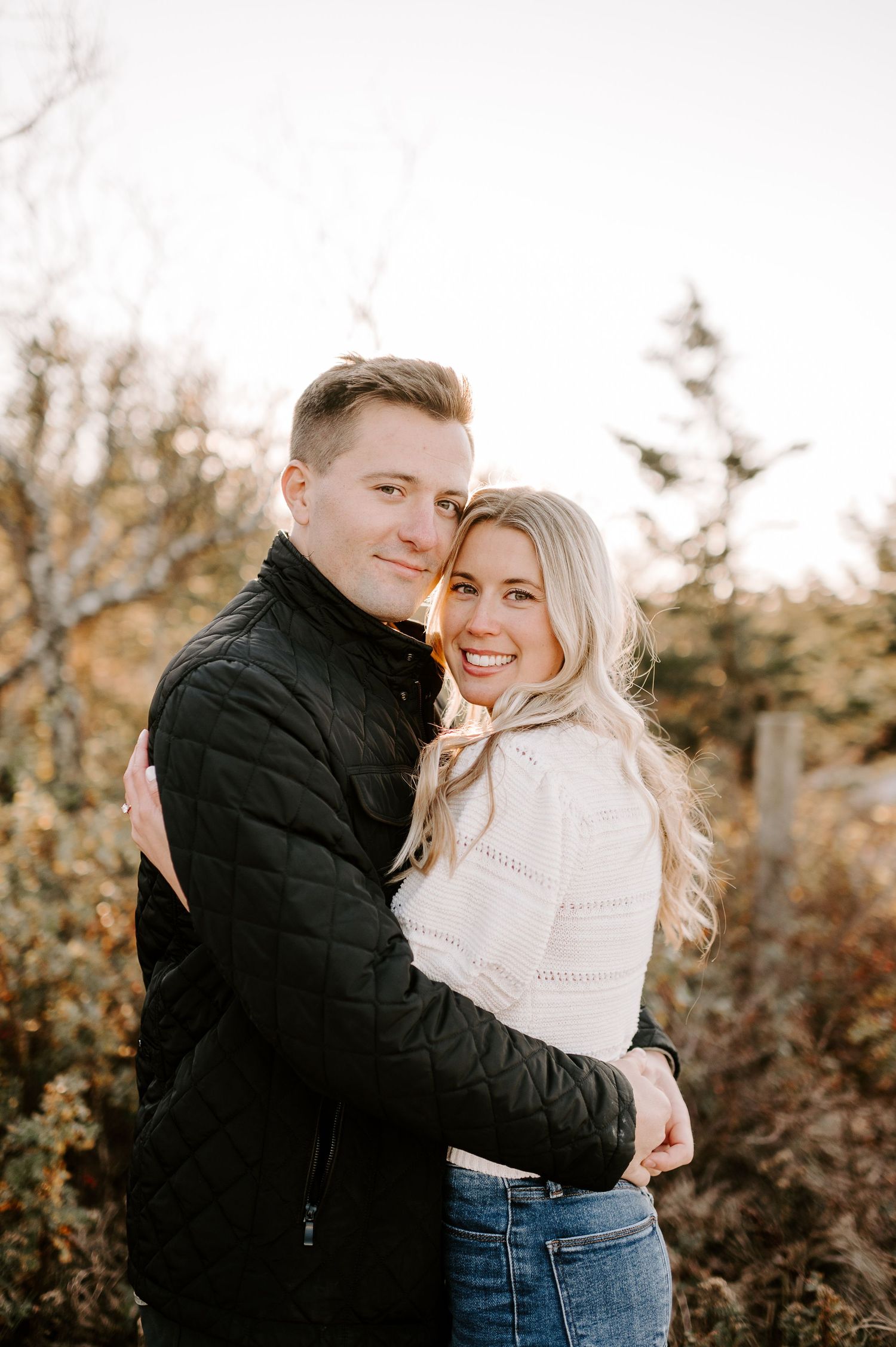 Couple embracing in warm sunlight against autumn foliage background.