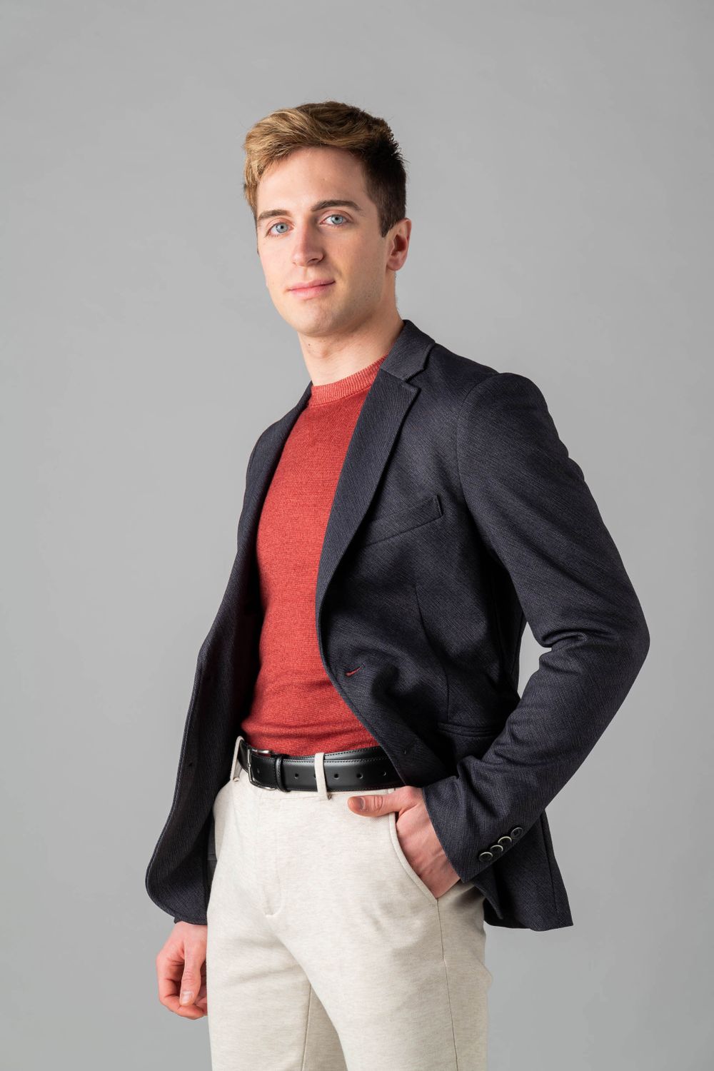 Business casual portrait of person in dark blazer and red shirt with light colored pants.