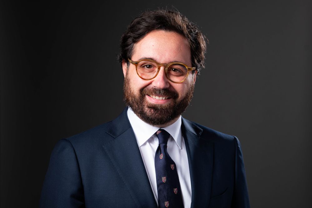 Professional portrait of smiling executive in glasses wearing navy suit and tie.