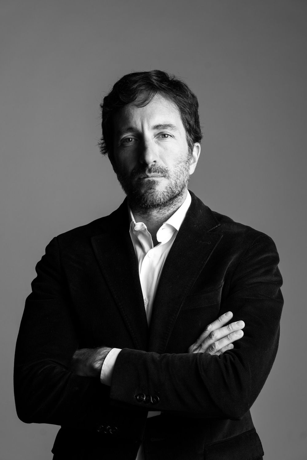 Black and white studio portrait of person in dark blazer with arms crossed.