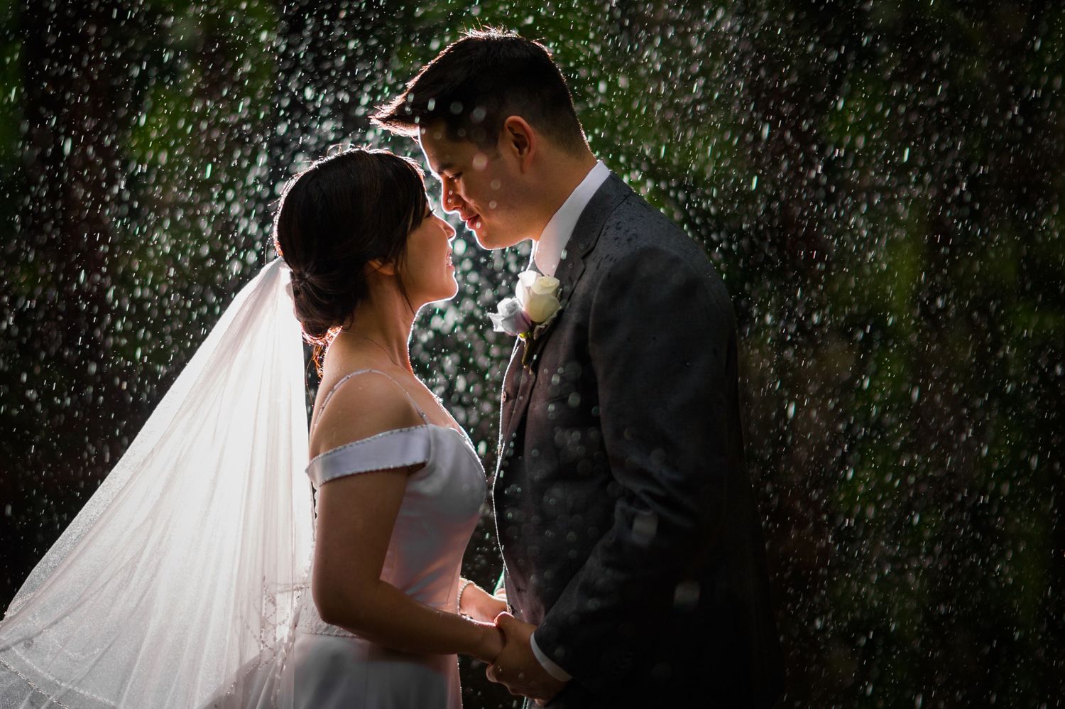 A romantic wedding portrait captured in the rain with falling water droplets.