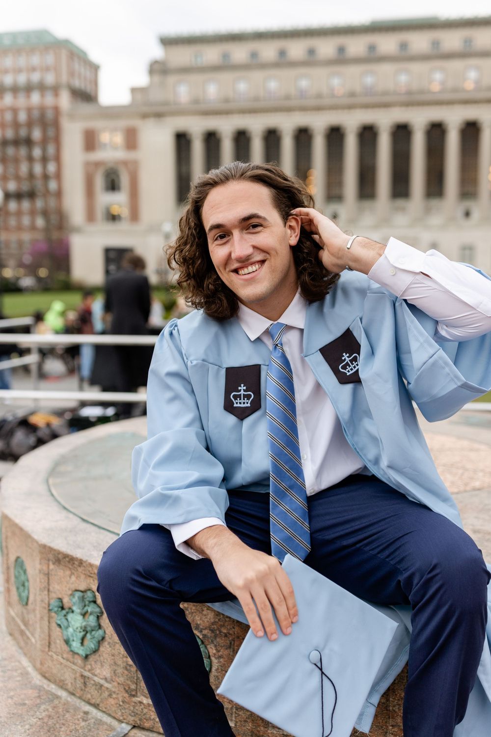 Graduate in Columbia University regalia poses on campus with classic architecture behind.