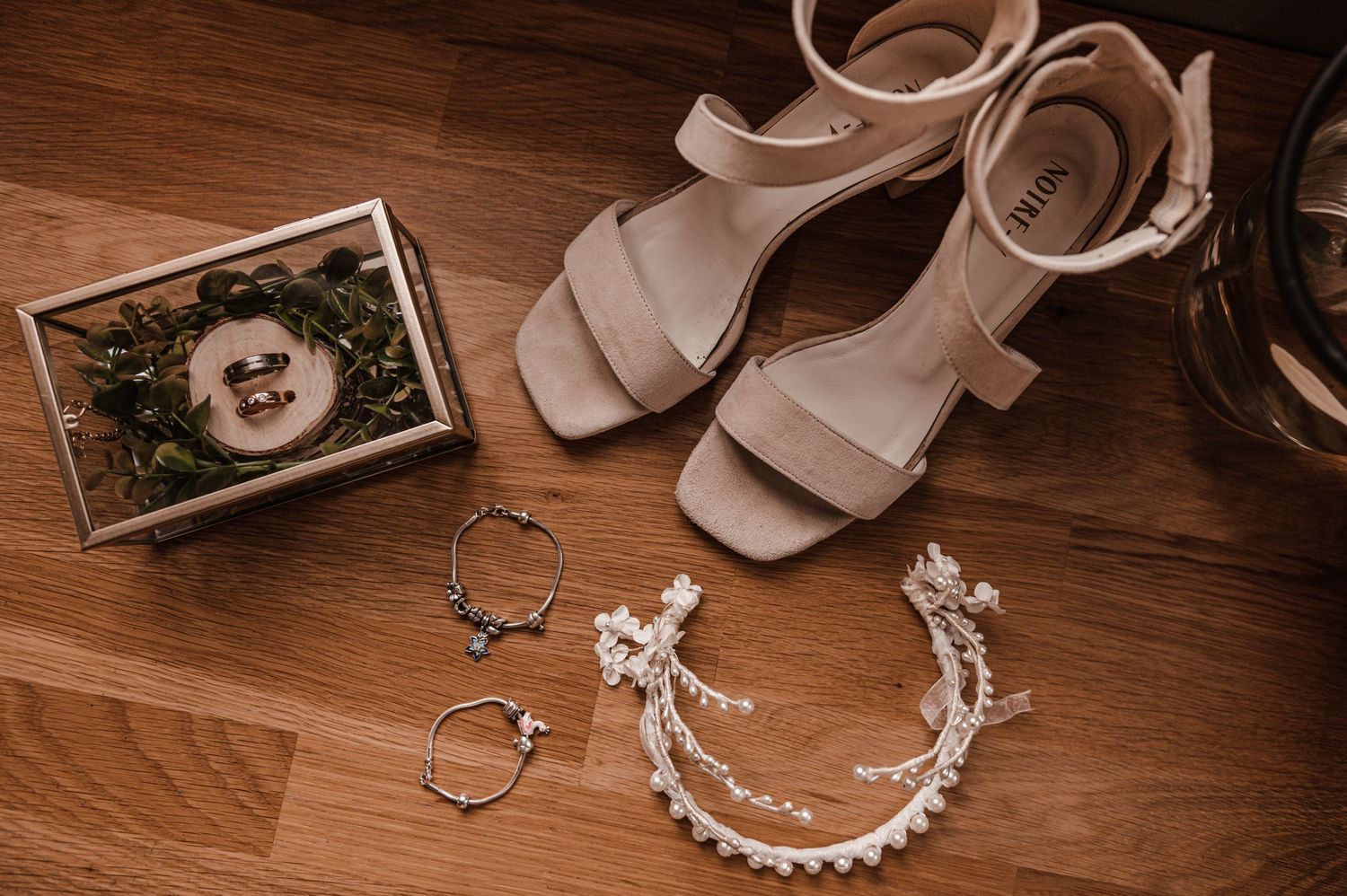 Wedding accessories and jewelry arranged on wooden surface in warm lighting.