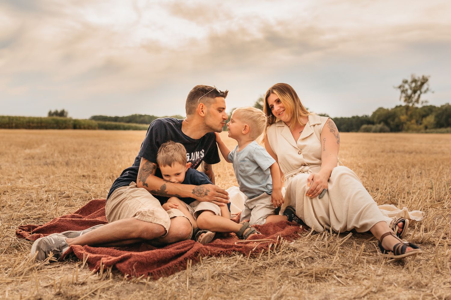Family relaxing together on a blanket in a golden wheat field.