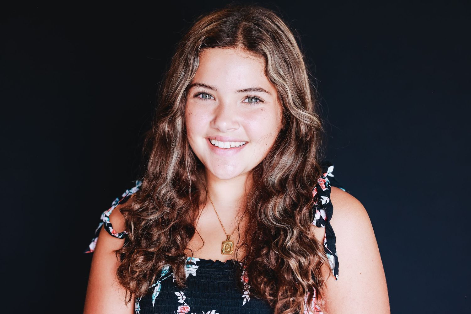 Portrait with natural curly hair wearing floral top against dark background.