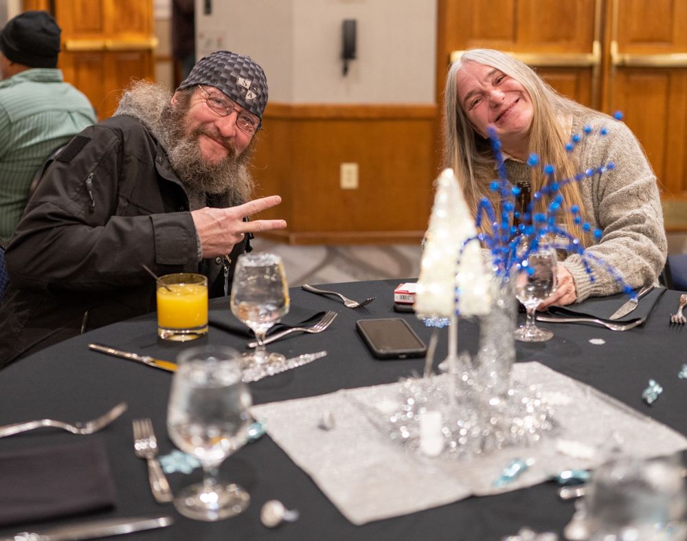 Two people share a laugh while sitting at a table with drinks and place settings in a dining room setting.