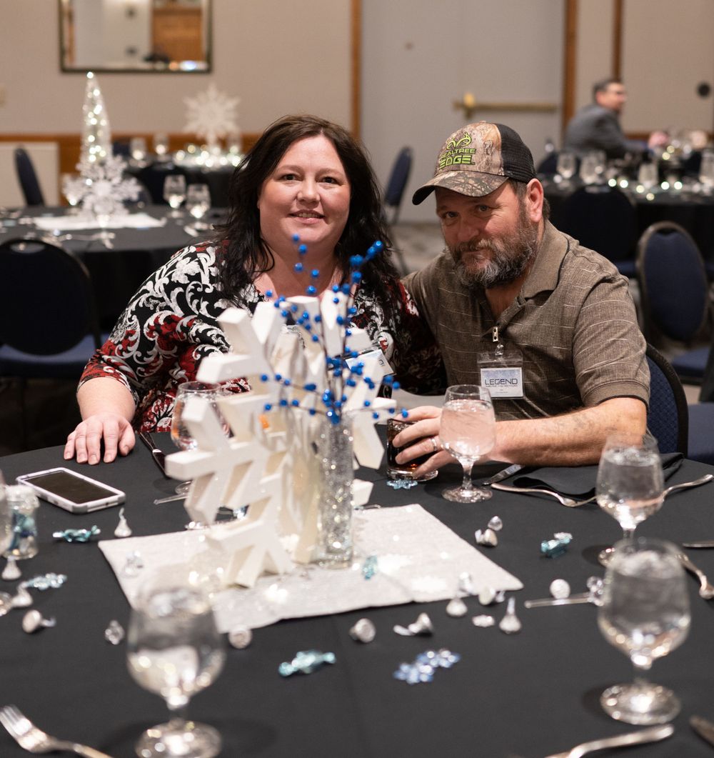 Two people work together at a decorated table with holiday centerpieces and scattered puzzle pieces at a formal event.