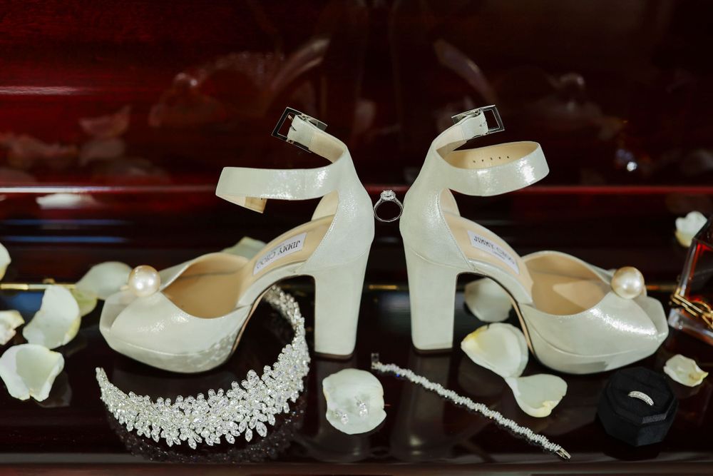 A row of elegant white bridal shoes with pearls and crystals displayed on a dark surface.