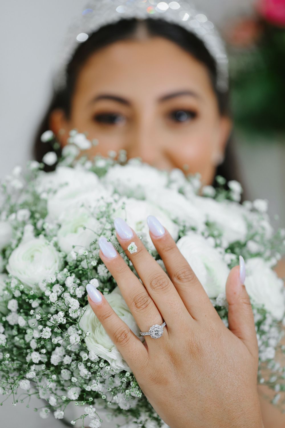 Close-up view of hands displaying an engagement ring against white baby's breath flowers in a bridal bouquet.