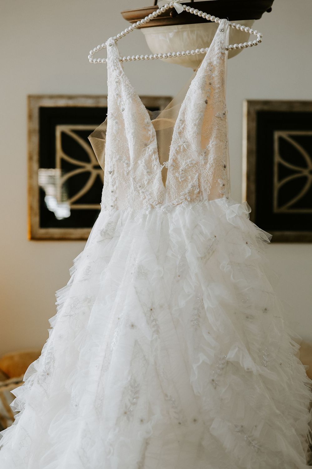 White wedding dress with lace details and tulle skirt hanging on display against neutral wall.