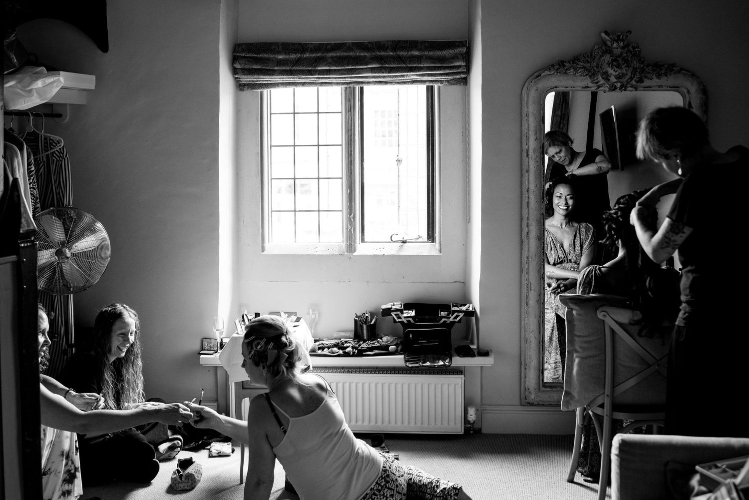 Black and white photo of getting ready moments in a sunlit room with mirror and window.