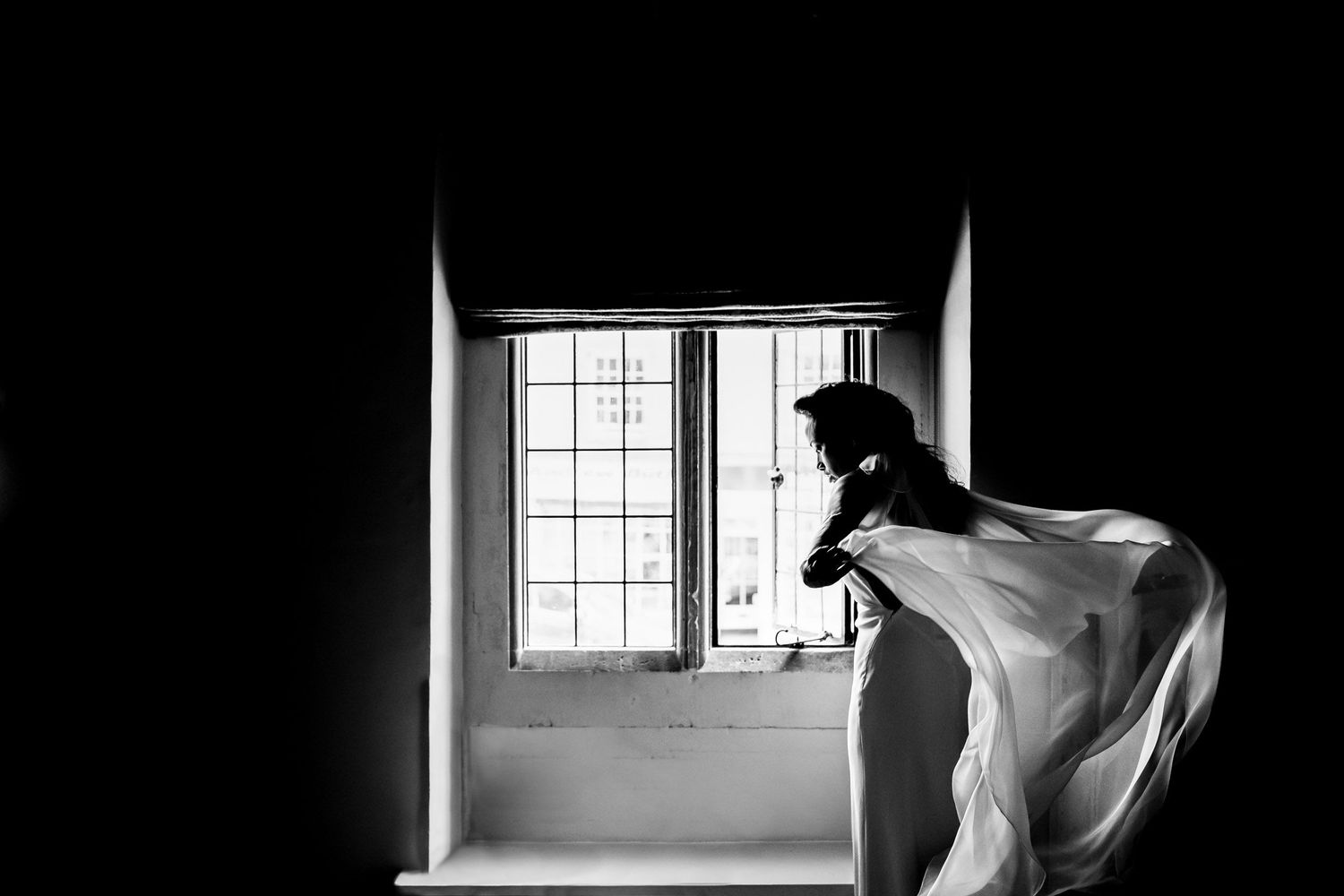 Dramatic black and white silhouette by window with flowing fabric.