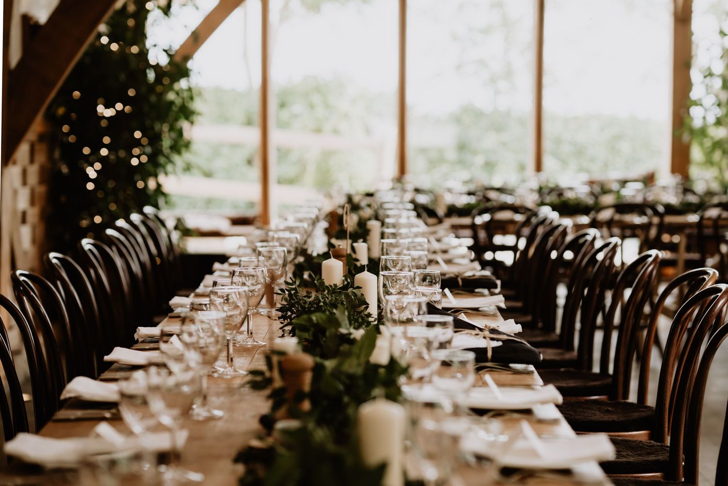 An elegant wedding reception table setting with floral centerpieces and dark wooden chairs.