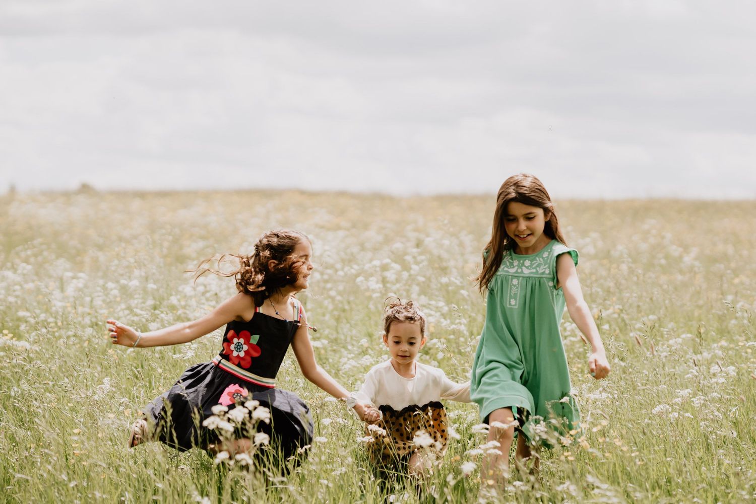 Three children playing together in a sunny wildflower meadow.