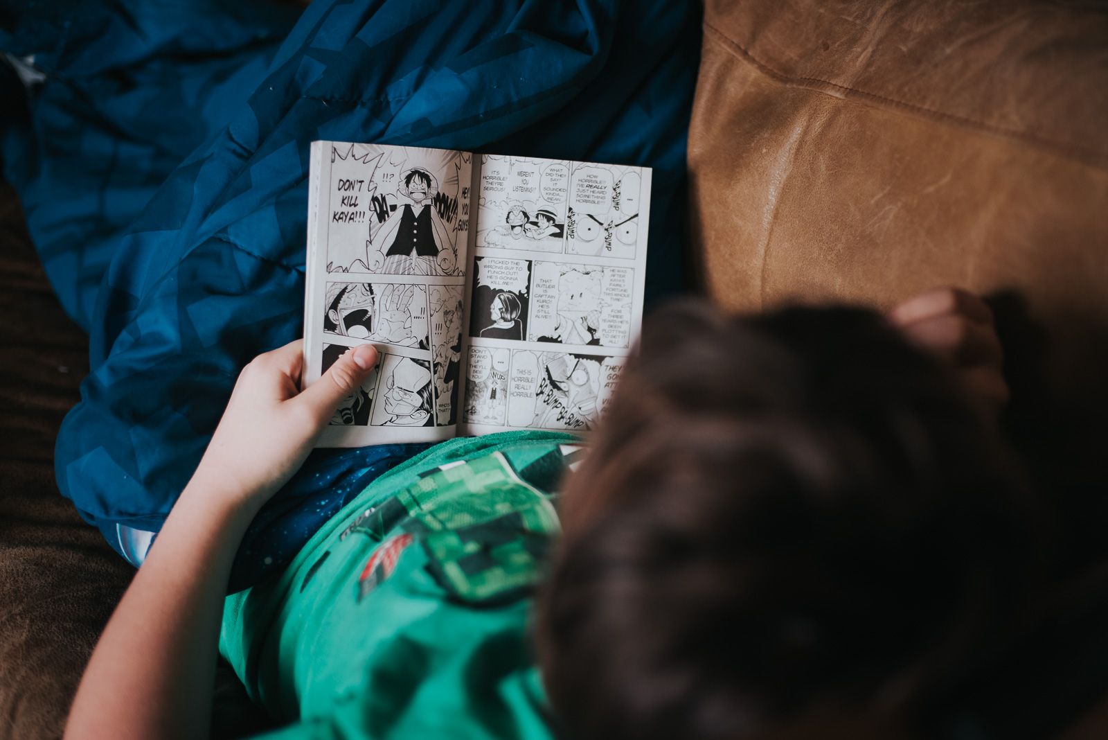 Looking over the should of a boy as he reads One Piece Graphic Novel while laying on the couch