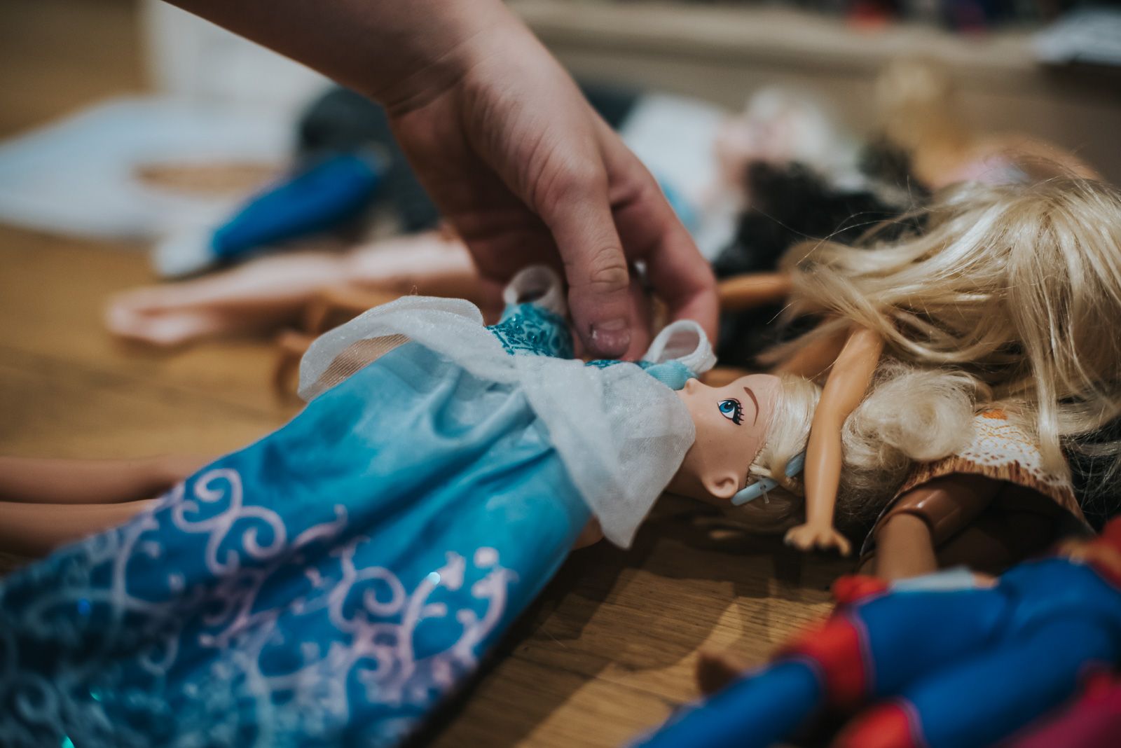 A blue doll dress is being lain over a Cinderella Barbie type doll.