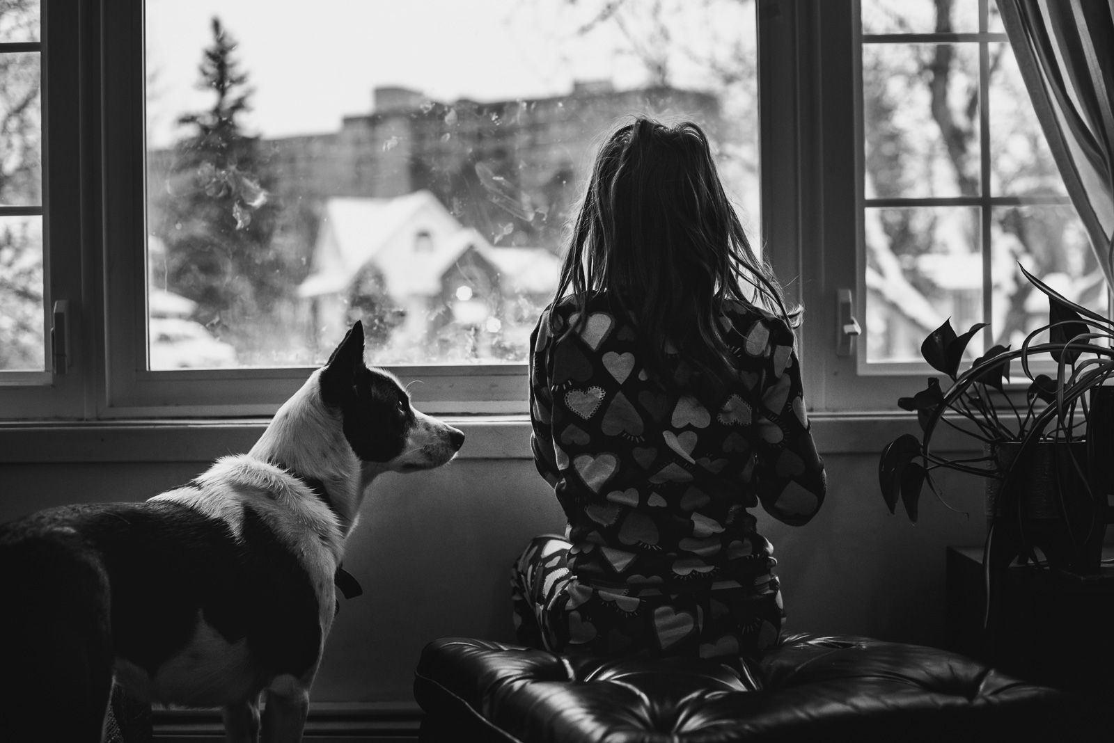 BW image of a girl looking out the window as her dog looks at her.