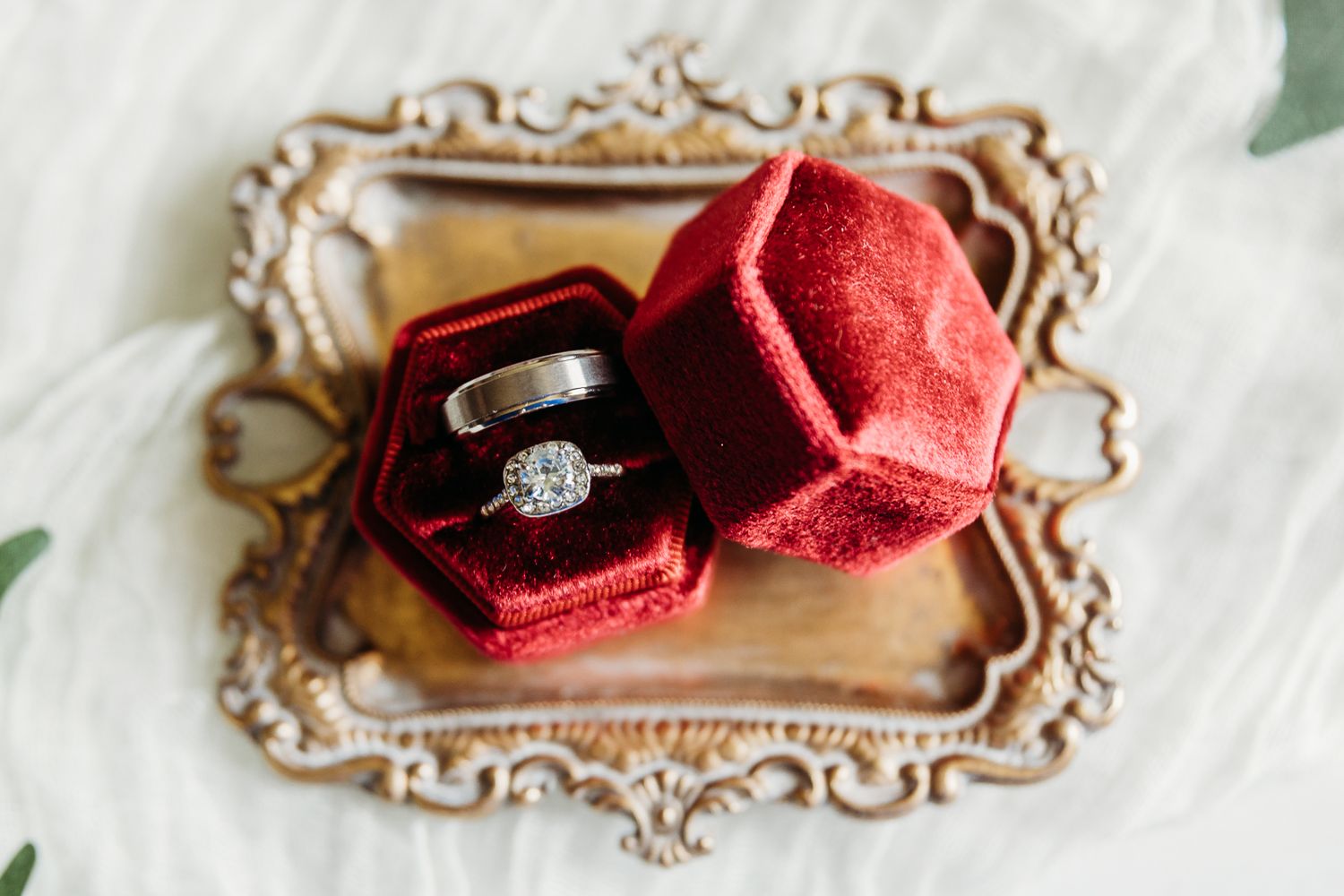 A sparkling diamond ring displayed in a red velvet box on an ornate gold tray.