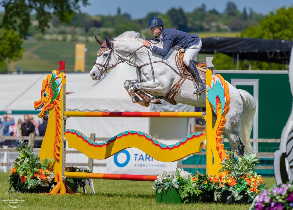 A horse and rider jumping over a colorfully decorated show jumping obstacle in a competition.