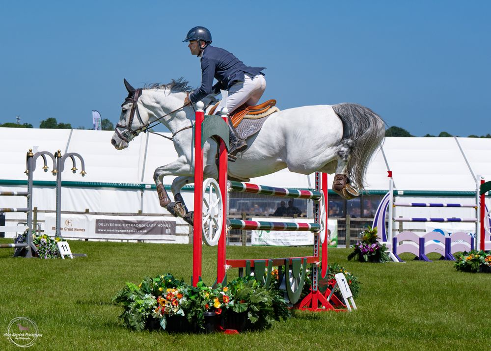 Equestrian athlete jumping over red and white obstacle during competition.