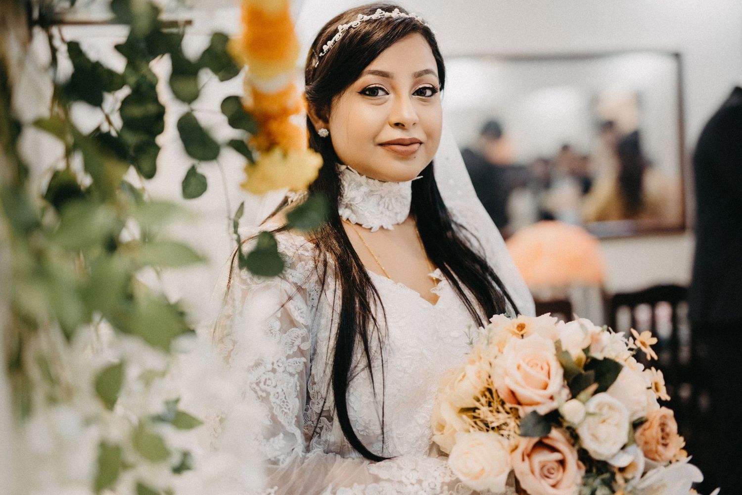 A bride holds a peach and cream rose bouquet while wearing a lace wedding dress.