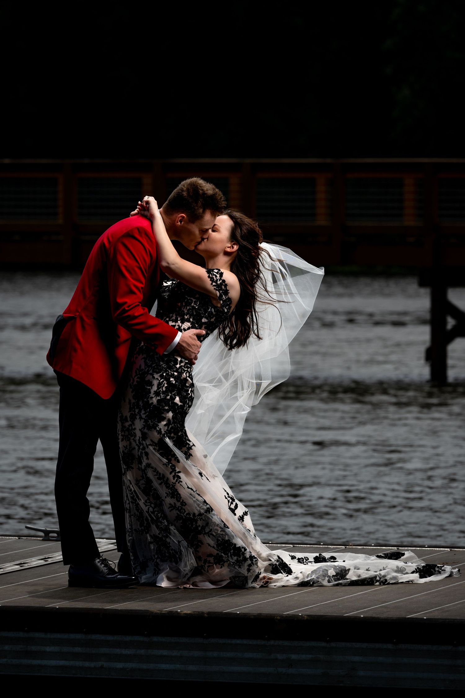 Romantic couple embracing on wooden dock over water in dramatic black and white composition.