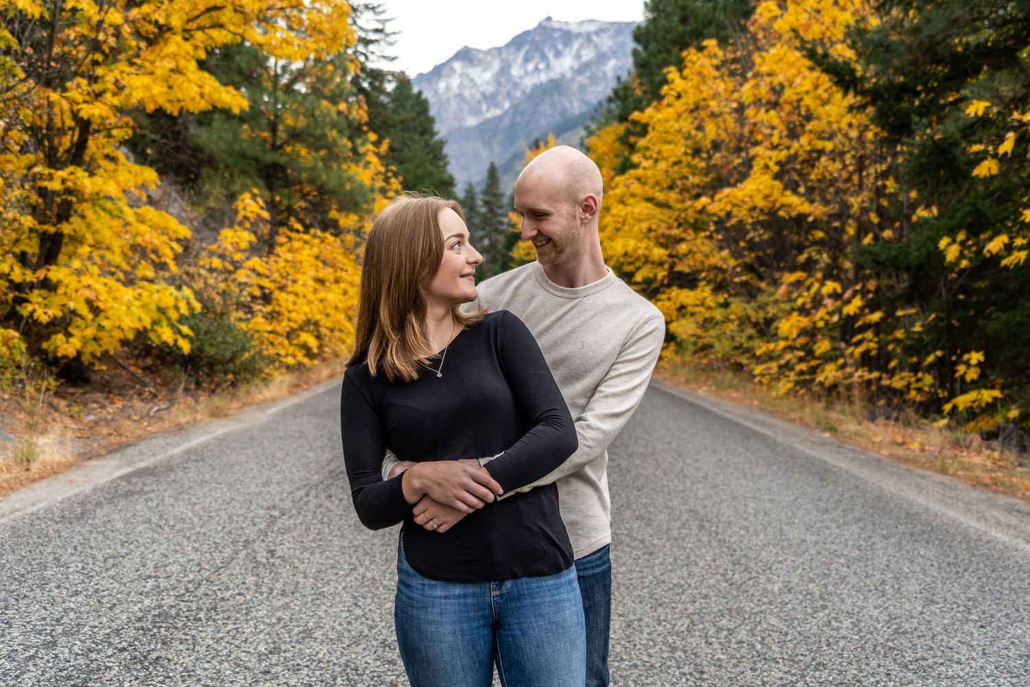A couple sharing an intimate moment on a road surrounded by fall foliage and mountain views.