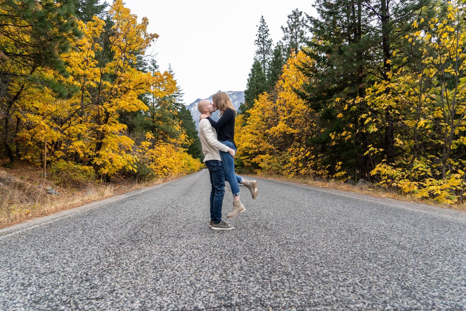 A couple embracing on a mountain road surrounded by vibrant autumn foliage.