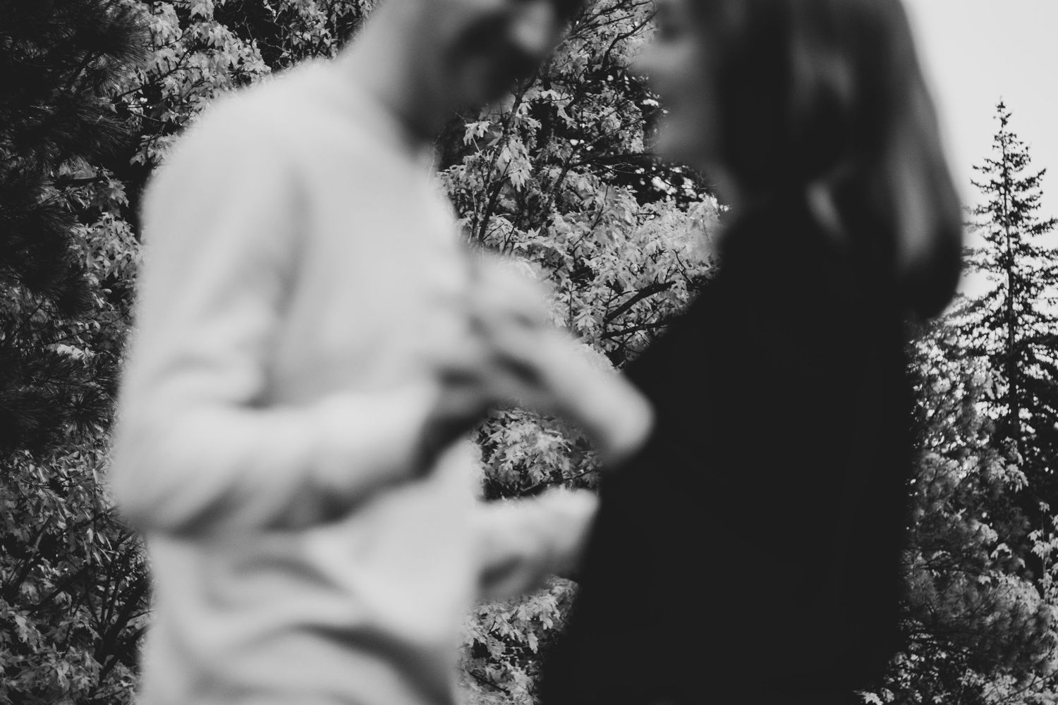 A black and white artistic photo of a couple sharing an intimate moment in nature.