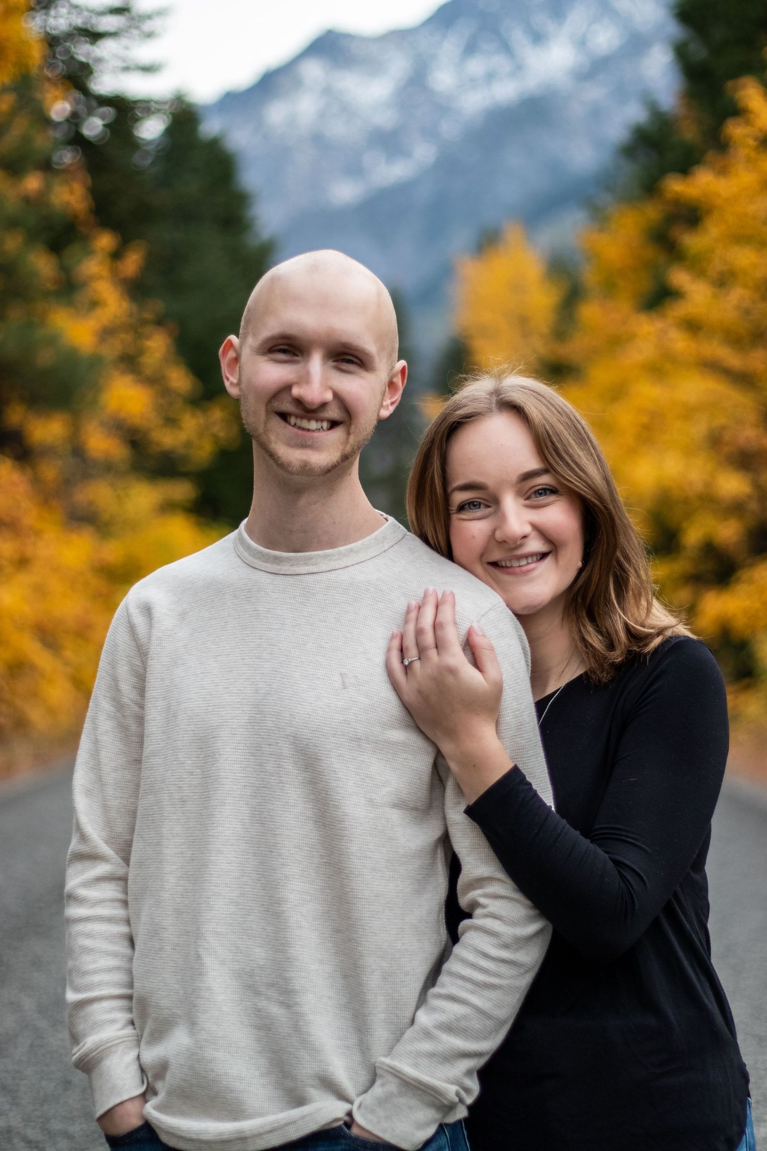 An affectionate couple posing on a mountain road with golden fall trees in the background.