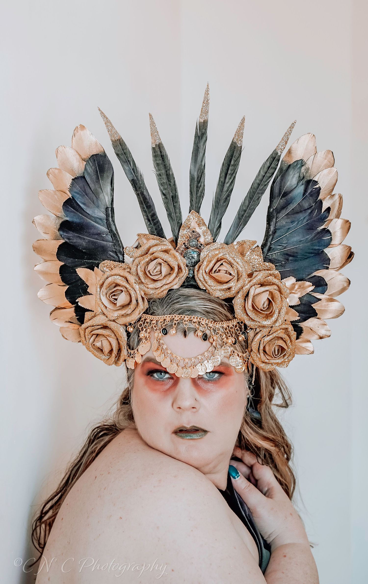 Artistic portrait featuring an ornate headdress with beige roses and black feathers against a light background.