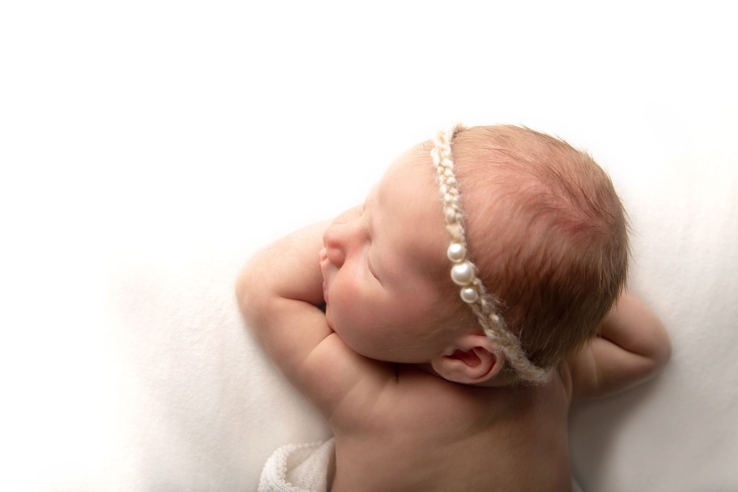 Newborn sleeping with her head resting on her folded arms with pearl headband. Vancouver Newborn photos