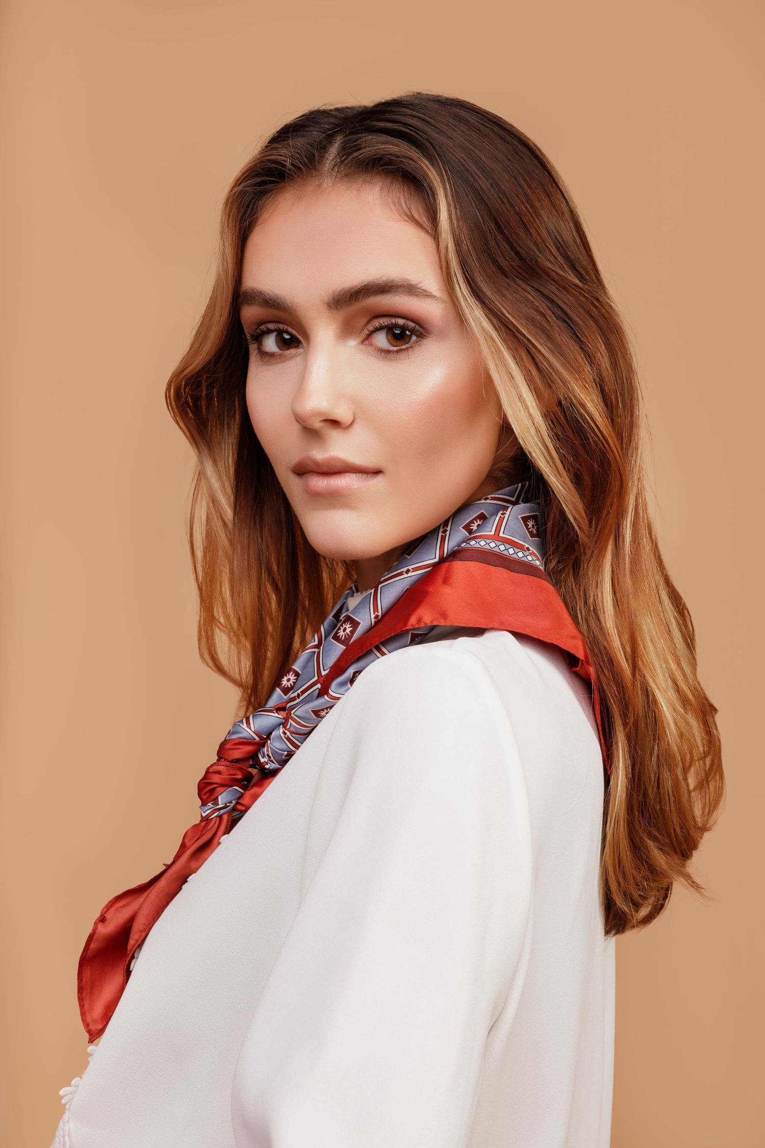 Portrait of model wearing white blouse with red and gray patterned silk scarf against neutral background.