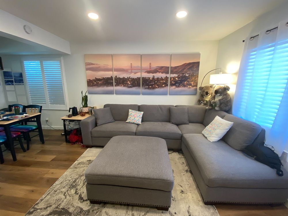 Contemporary living room with grey sectional sofa and multi-panel sunset cityscape artwork.