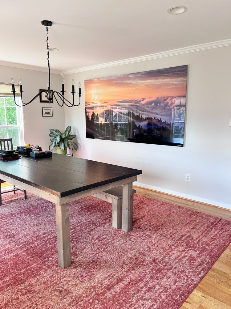 Modern dining room with black chandelier and scenic fog landscape artwork on white wall.