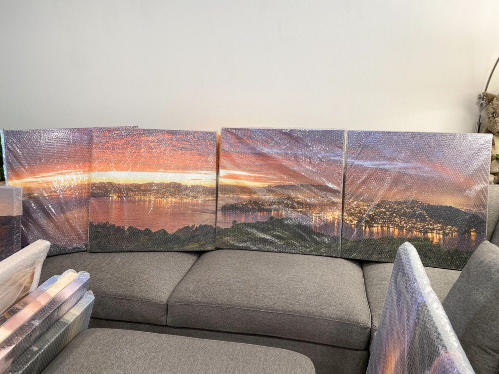 Multi-panel canvas prints of a scenic sunset view laid out on a grey couch.