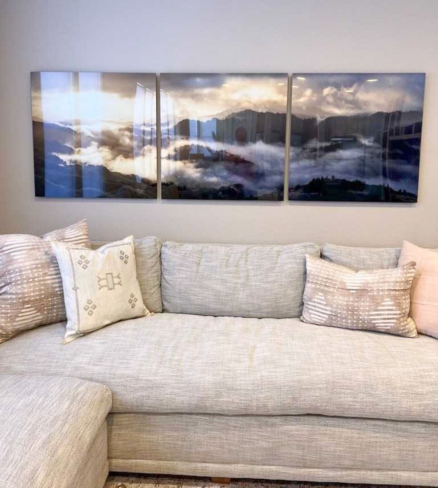 Modern living room featuring three-panel misty mountain landscape artwork above sectional couch.
