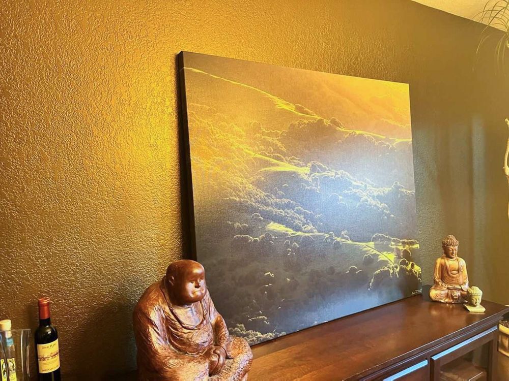 Golden sunset canvas print displayed on dark wall with Buddha statue decoration.