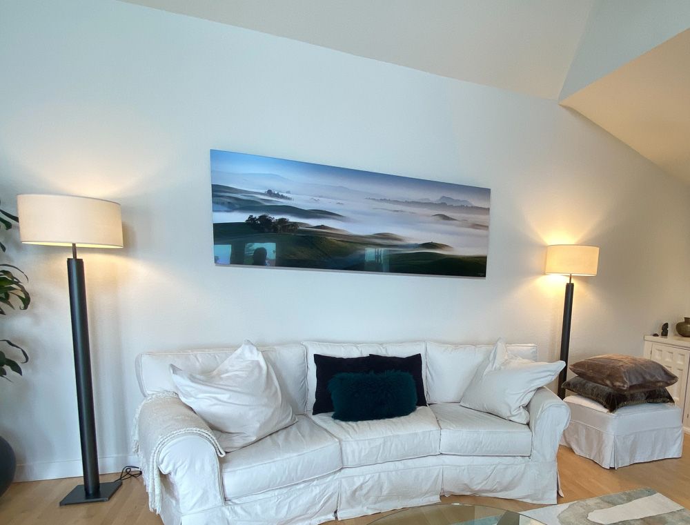 Serene coastal landscape canvas print mounted above white couch with floor lamps.