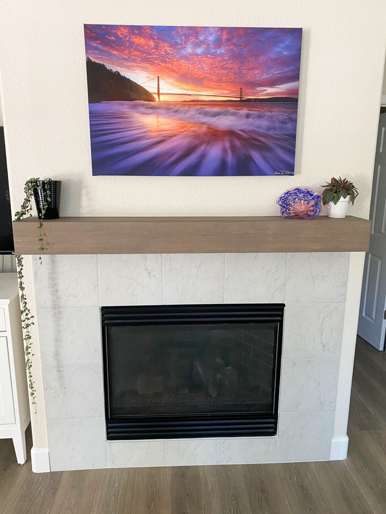 Modern fireplace with a vibrant sunset and Golden Gate Bridge canvas print mounted above wooden mantel.