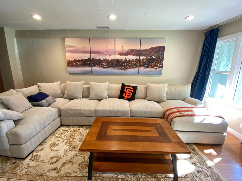 Spacious living room featuring large sectional sofa and panoramic cityscape artwork above.